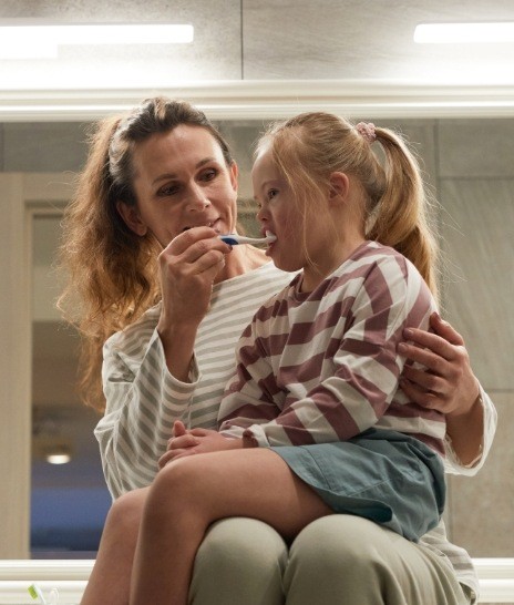 Mother helping her daughter brush her teeth