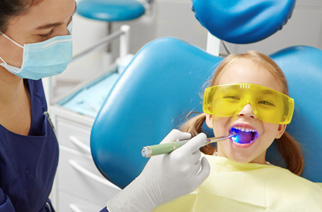 Dentist shining UV light on little girl’s dental treatment
