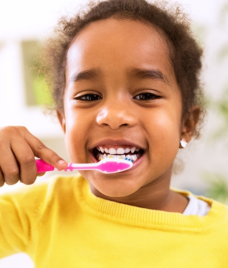 young girl smiling while brushing teeth 