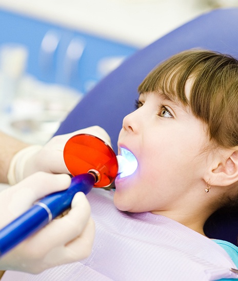 Hands applying UV light to girl’s dental filling