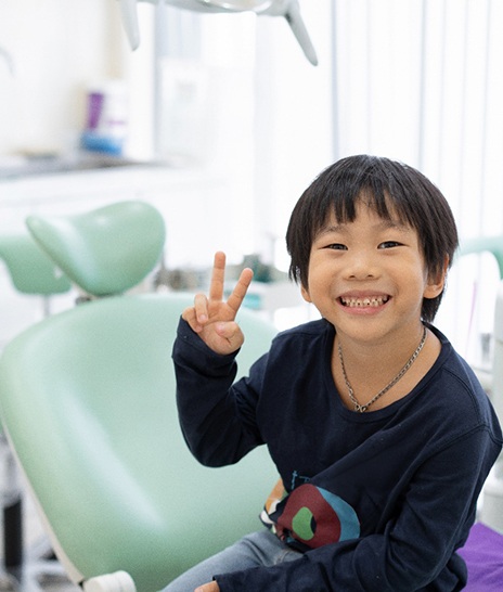 Little boy in dental chair smiling giving peace sign