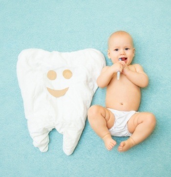 Baby holding toothbrush and laying next to tooth shaped blanket