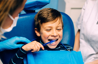 Child smiling while brushing their teeth with dentist