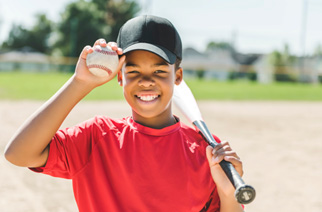 Child smiling with baseball and baseball bat on field