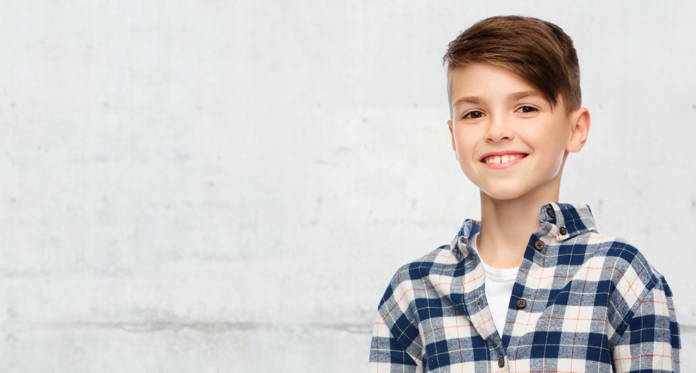 Young boy in plaid shirt smiling after restorative dentistry for kids