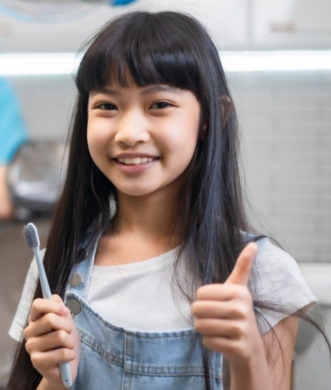 Young girl holding toothbrush and giving thumbs up