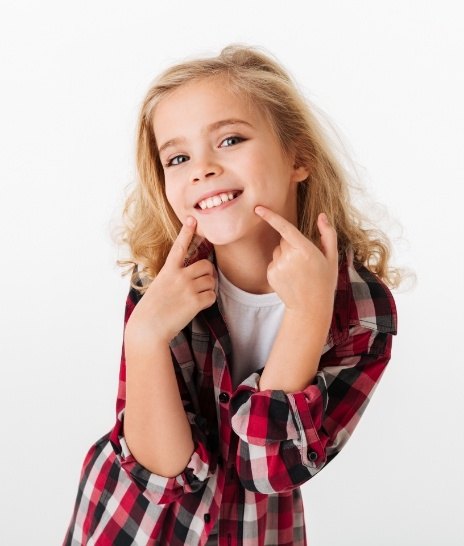 Young girl in red plaid shirt pointing to her smile