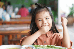a child smiling while eating lunch at school