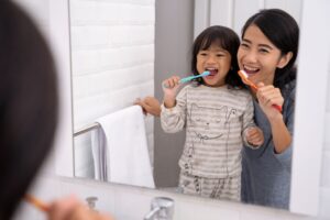 Woman with little girl at bathroom mirror brushing teeth together